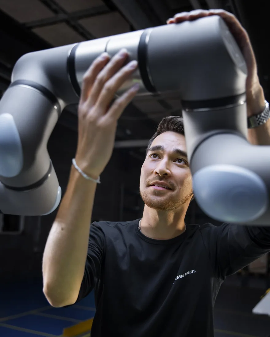 Técnico guiando com as mãos o braço de um robô colaborativo da Universal Robots