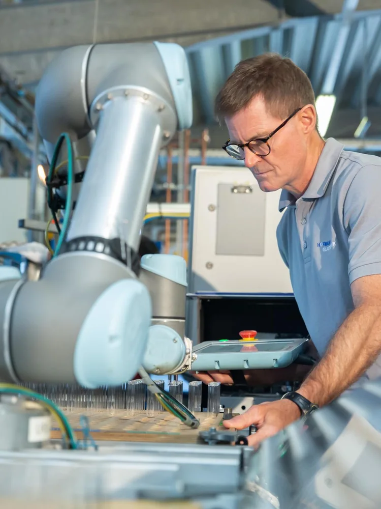 Técnico e robô colaborativo da Universal Robots trabalhando numa bancada com peças